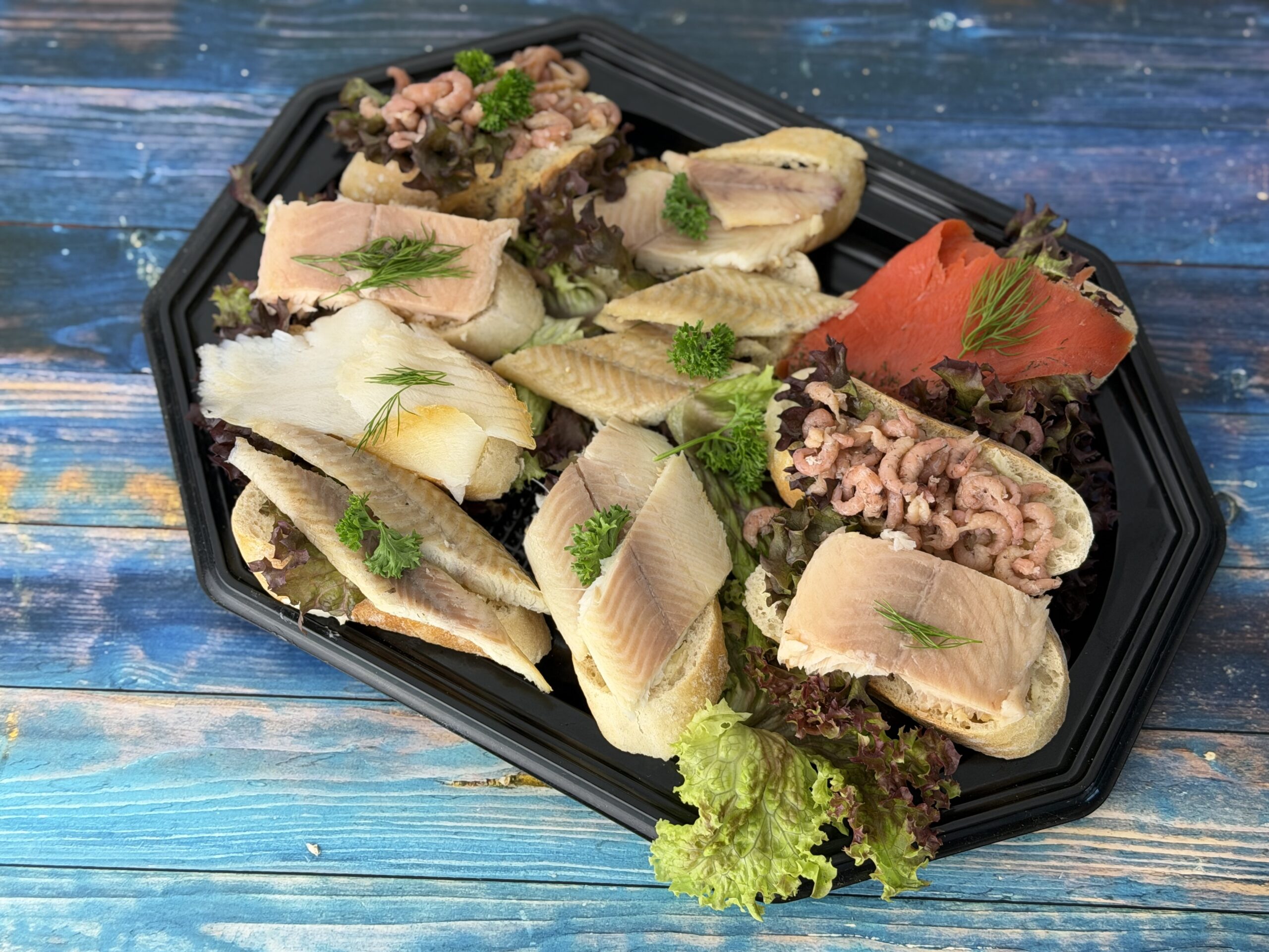 Canapés mit Baguette-Häppchen aus Räucherlachs, Räucherfisch, Nordseekrabben und Graved-Sockeye-Lachs auf schwarzem Tablett