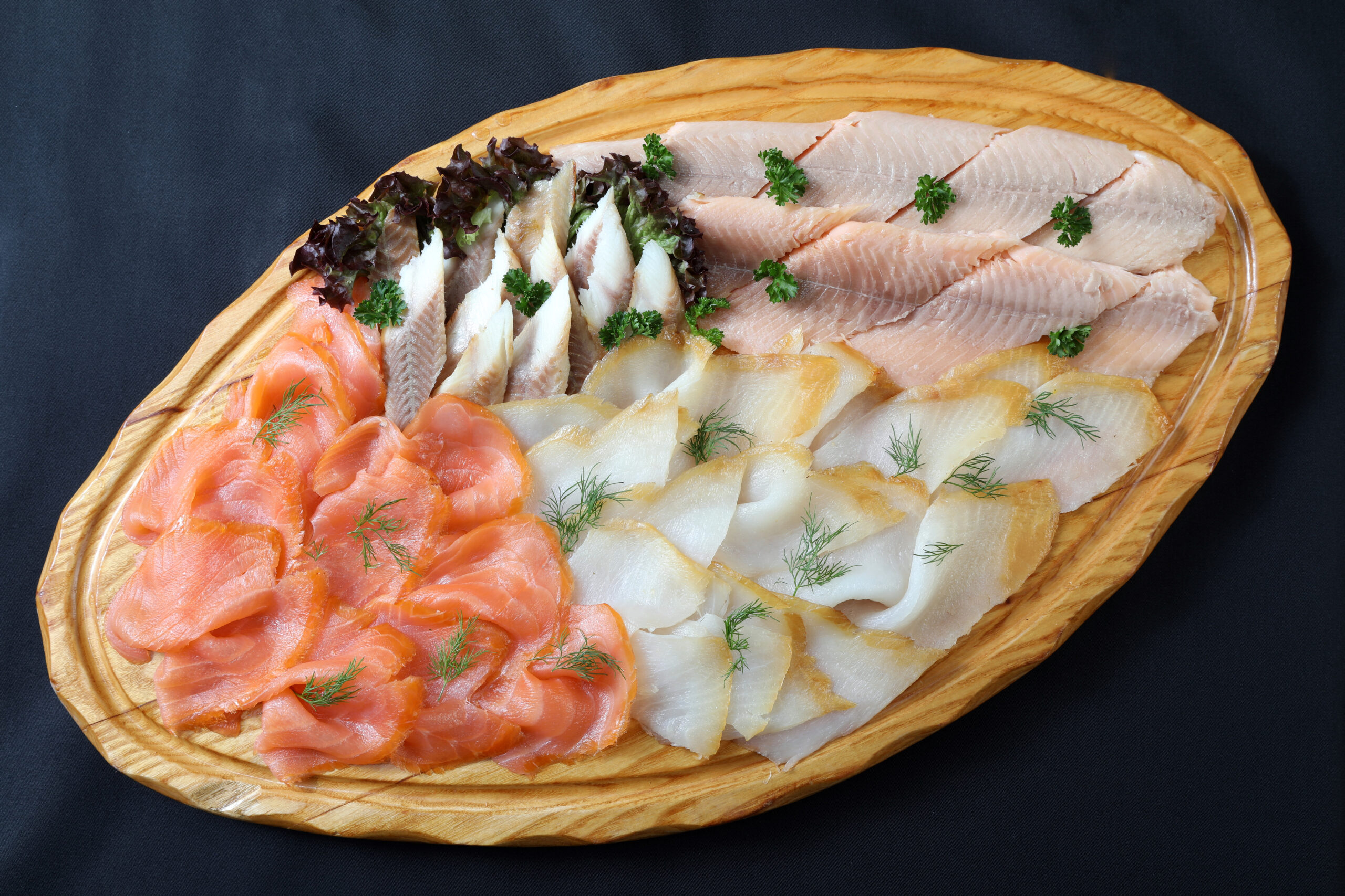 Edelfischplatte mit irischem Lachs, Lachsforellen-Filet, Lachs-Butt und Räucher-Aal-Filet auf ovalem Holzbrett