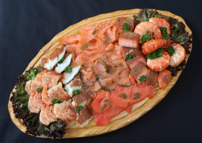 Königsplatte mit Lachsvielfalt, Räucherfisch, Garnelen und Riesengarnelenschwänzen auf ovalem Holzbrett