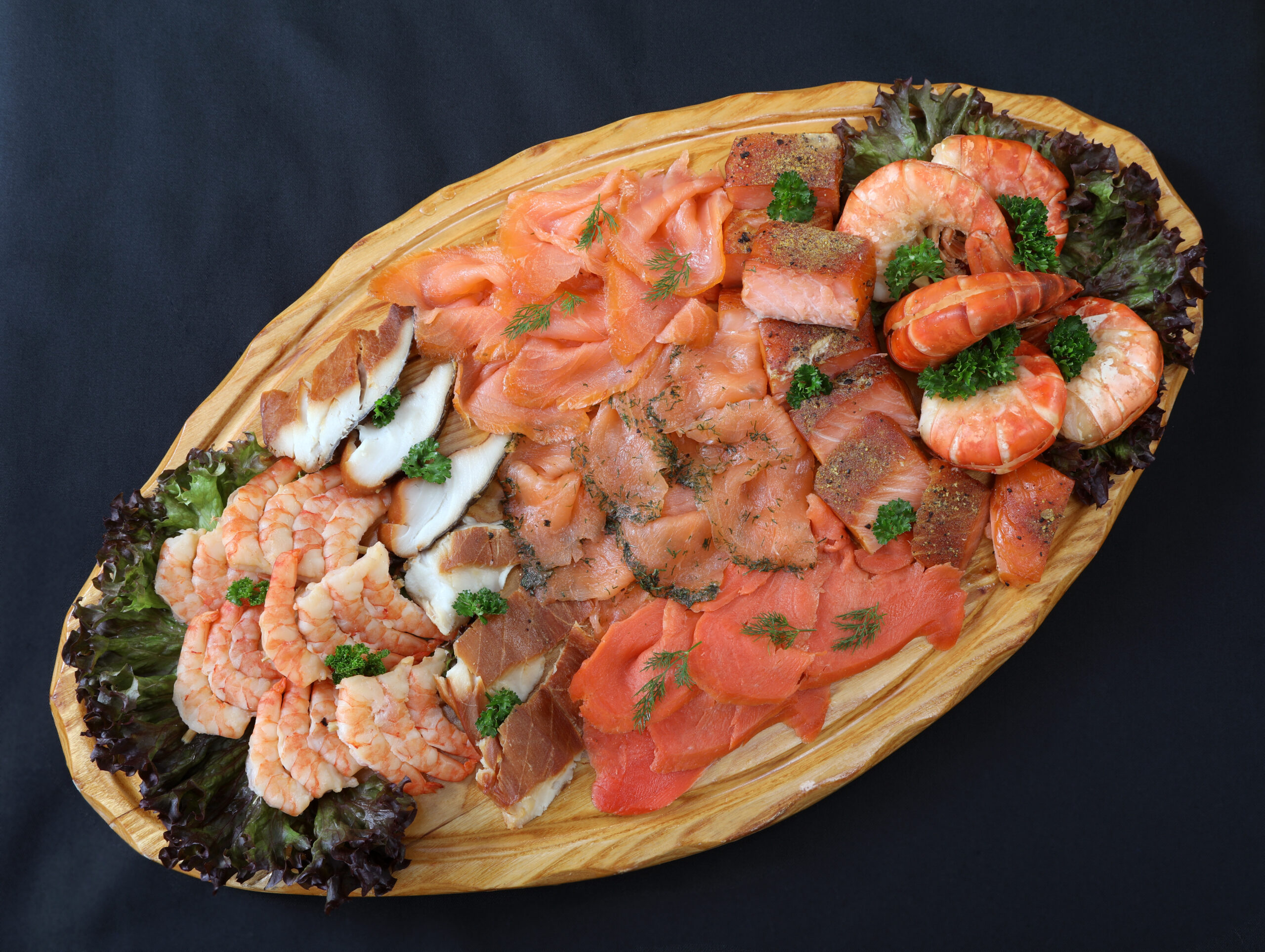 Königsplatte mit Lachsvielfalt, Räucherfisch, Garnelen und Riesengarnelenschwänzen auf ovalem Holzbrett
