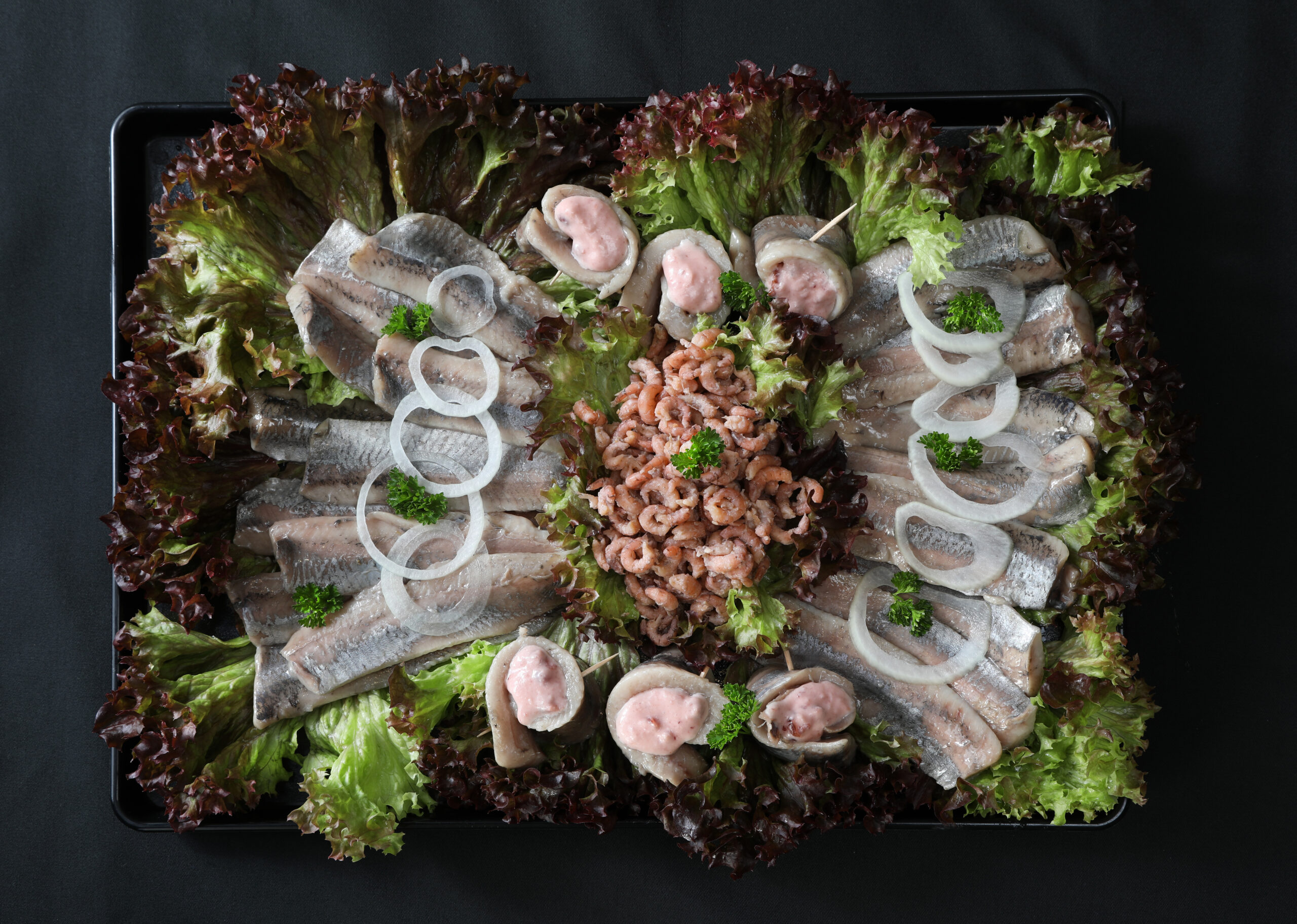 Matjesplatte mit Matjesfilets, gefüllten Matjes-Röllchen mit Preiselbeeren und Nordsee-Krabbenfleisch auf schwarzem Tablett