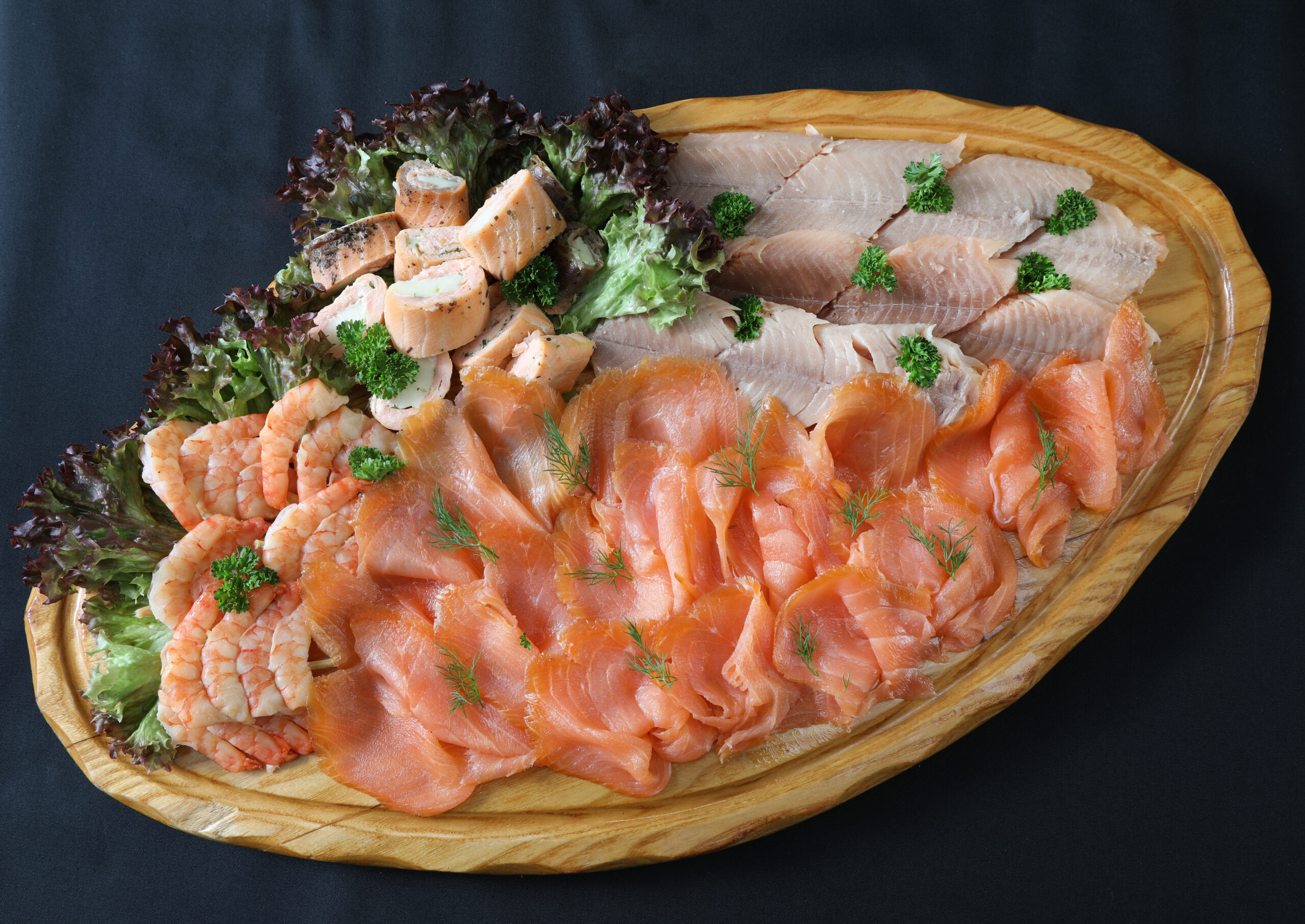 Fischplatte "Vom Feinsten" mit Saiblingsfilet, Clare-Island-Räucherlachs, Lachsrouladen und Garnelen auf ovalem Holzbrett