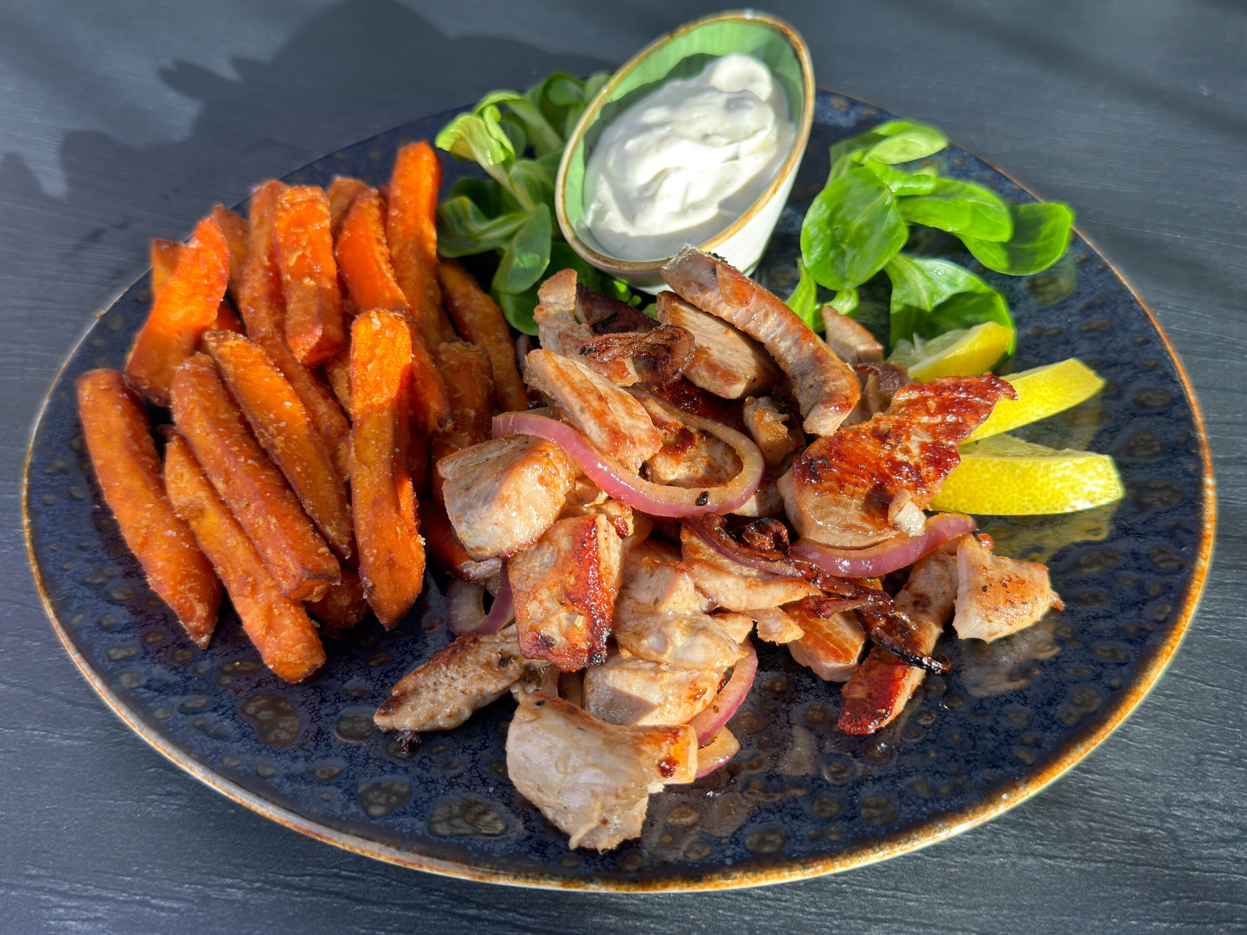 Thunfisch-Gyros mit Süßkartoffelpommes, rotem Zwiebeln, Feldsalat, Zitronenspalten und Dip auf dunklem Teller – Gericht der Wuppertaler Fischkultur